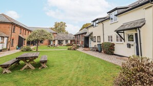 A courtyard with a picnic table, a small garden, and a building with a door and windows. - Rushmoor Cottage (Sidmouth)