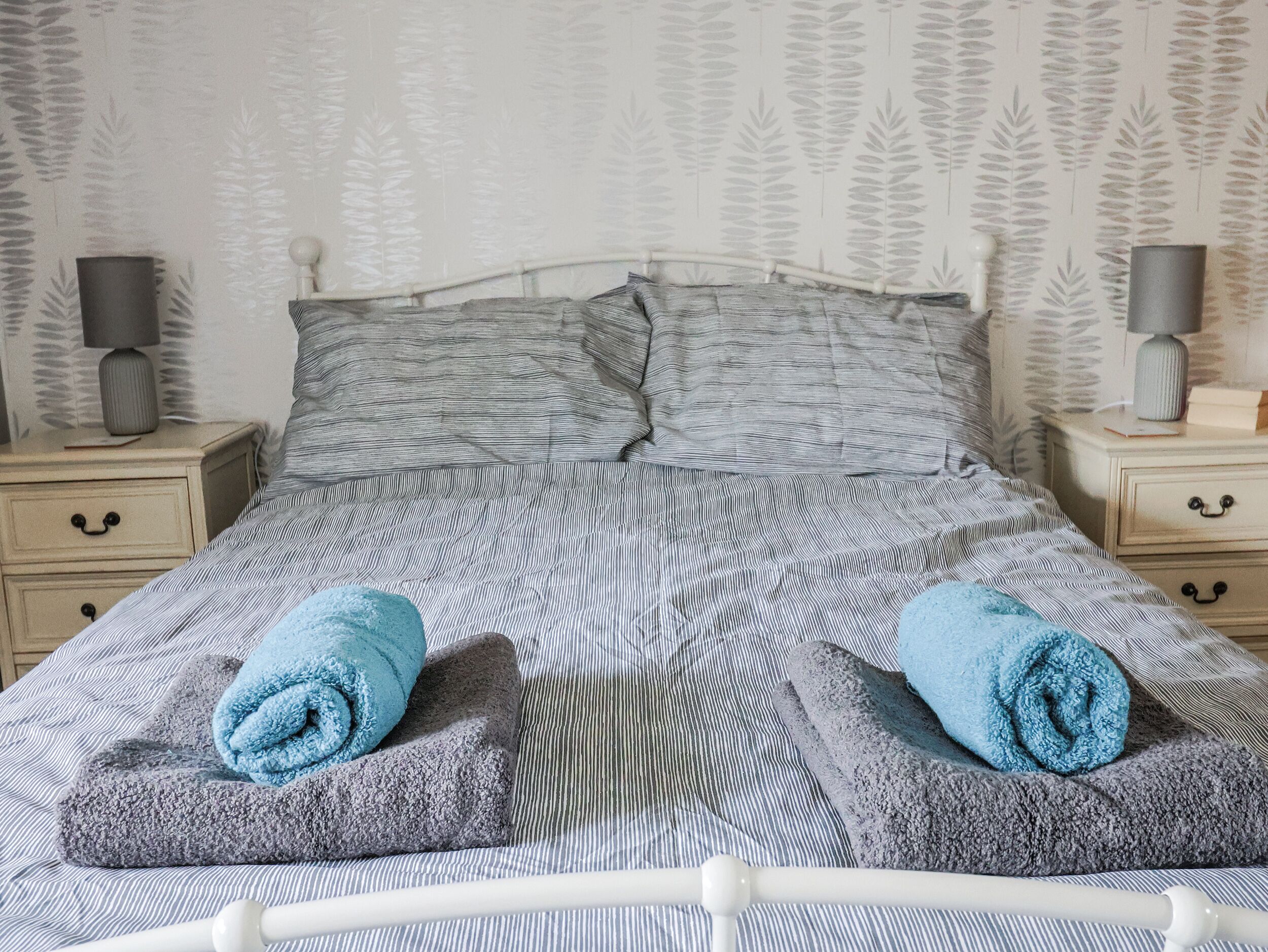 A neatly made bed with striped bedding and two rolled towels.