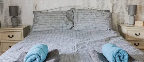 A neatly made bed with striped bedding and two rolled towels.
