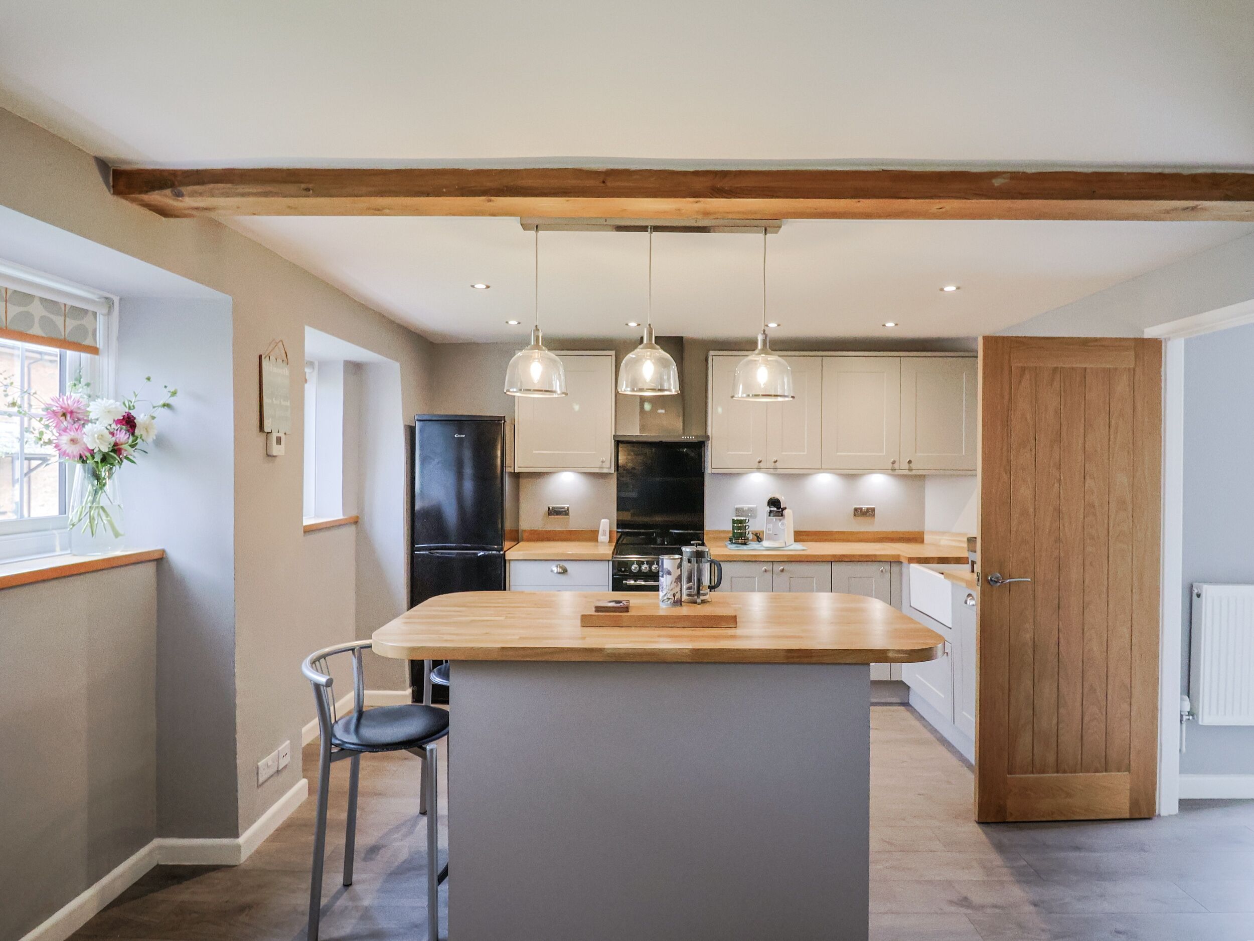 A modern kitchen with a central island, pendant lighting, and wooden beams on the ceiling.
