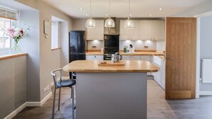 A modern kitchen with a central island, pendant lighting, and wooden beams on the ceiling. - Rushmoor Cottage (Sidmouth)