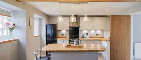 A modern kitchen with a central island, pendant lighting, and wooden beams on the ceiling.