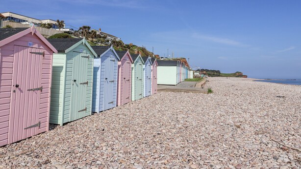 A row of colorful beach huts with a pebble beach and a clear sky. - Rushmoor Cottage (Sidmouth)