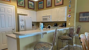 A kitchen with white cabinets, a refrigerator, a microwave, and a bar area with wicker chairs.