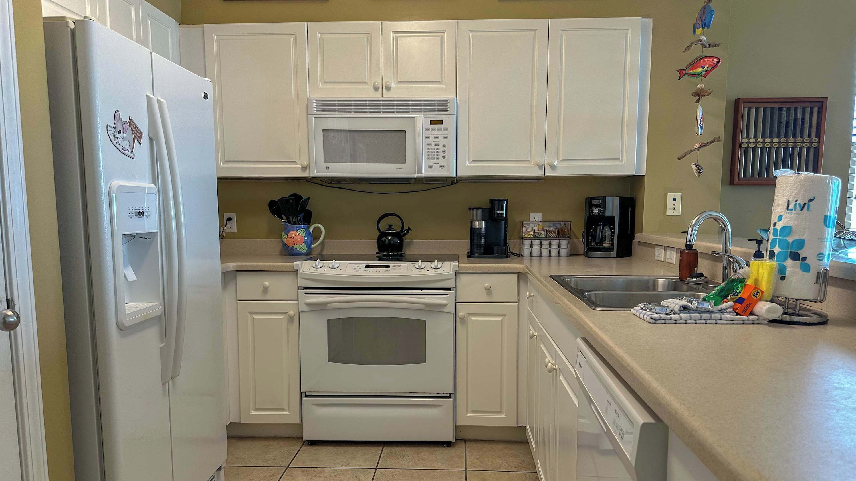A kitchen with white cabinets, a microwave, a stove, a dishwasher, and various kitchen items on the counter.