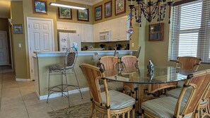 A kitchen with white cabinets, a refrigerator, a microwave, and a dining area with a glass table and wicker chairs.