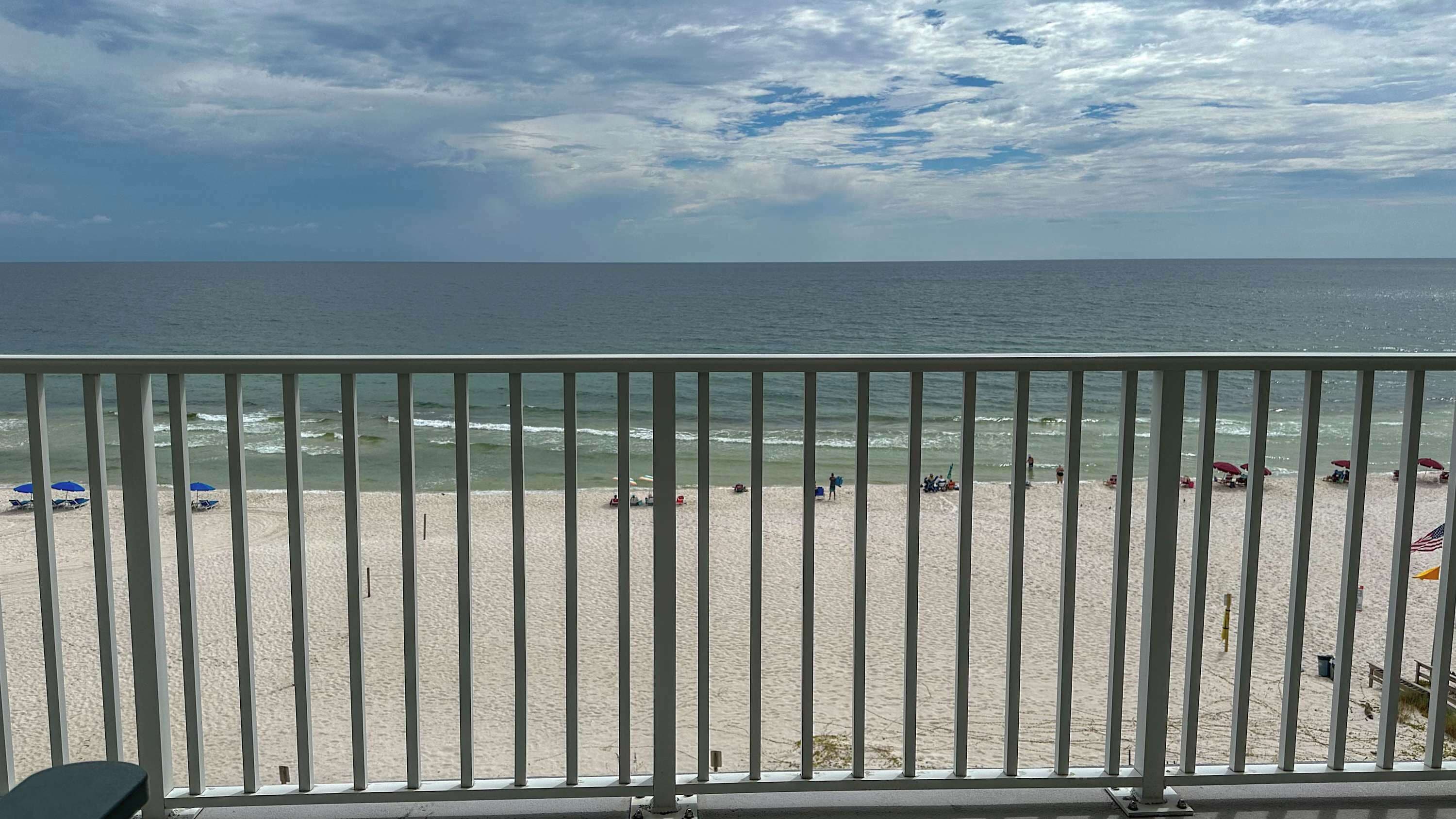 Ein Strand mit einem Metallgeländer im Vordergrund, ein sandiger Strand und das Meer im Hintergrund.