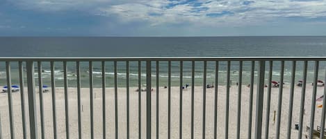 A beach with a metal railing in the foreground, a sandy beach, and the ocean in the background.