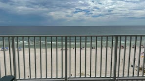 A beach with a metal railing in the foreground, a sandy beach, and the ocean in the background.