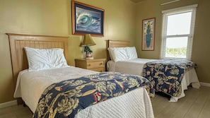 A bedroom with two beds, a nightstand with a lamp, and a window with blinds.