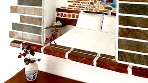 Ein Schlafzimmer mit einem Kopfende aus Ziegelsteinoptik, einem weißen Bett und einem Spiegel mit Sonnendesign.