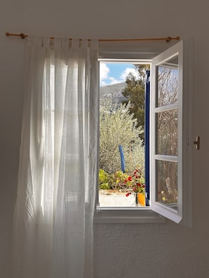 An open window with a view of a garden and a mountain. - Jasmine of Cyclades (Syros)