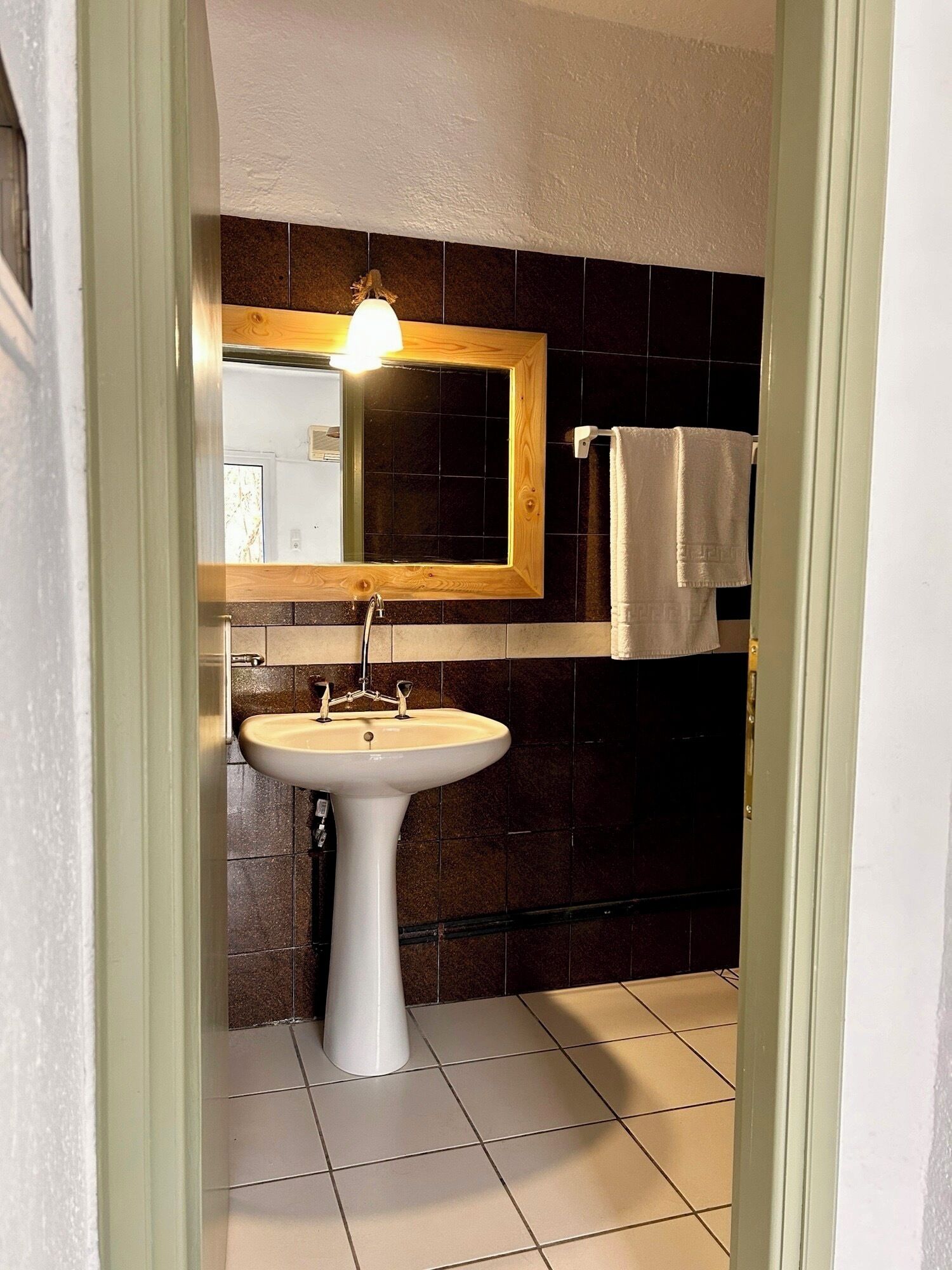 Un baño con un lavabo blanco, un espejo con marco de madera y paredes de baldosas oscuras.