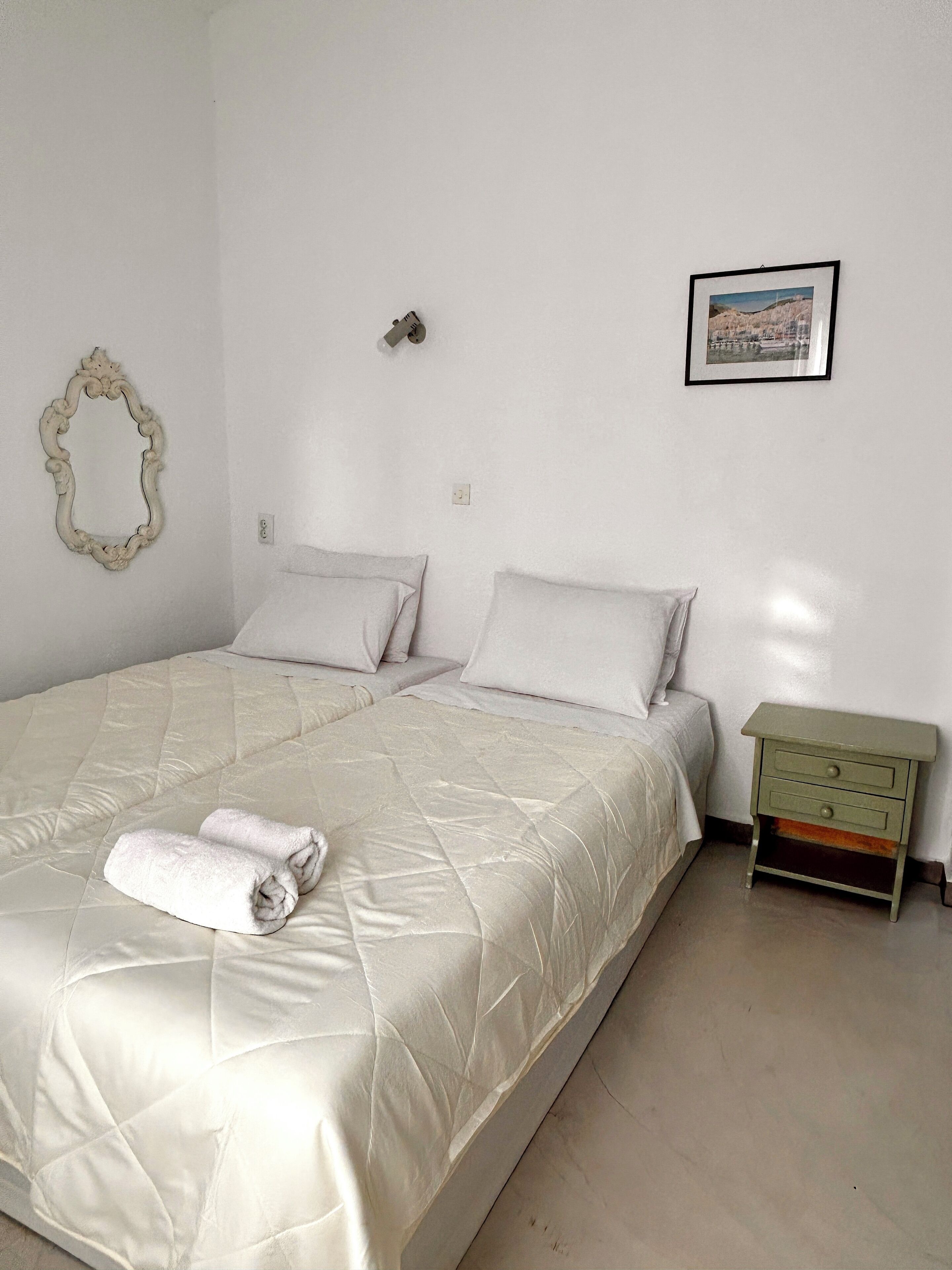 A double bed with a quilted duvet, a small bedside table, a wall-mounted mirror, and a framed picture on the wall.