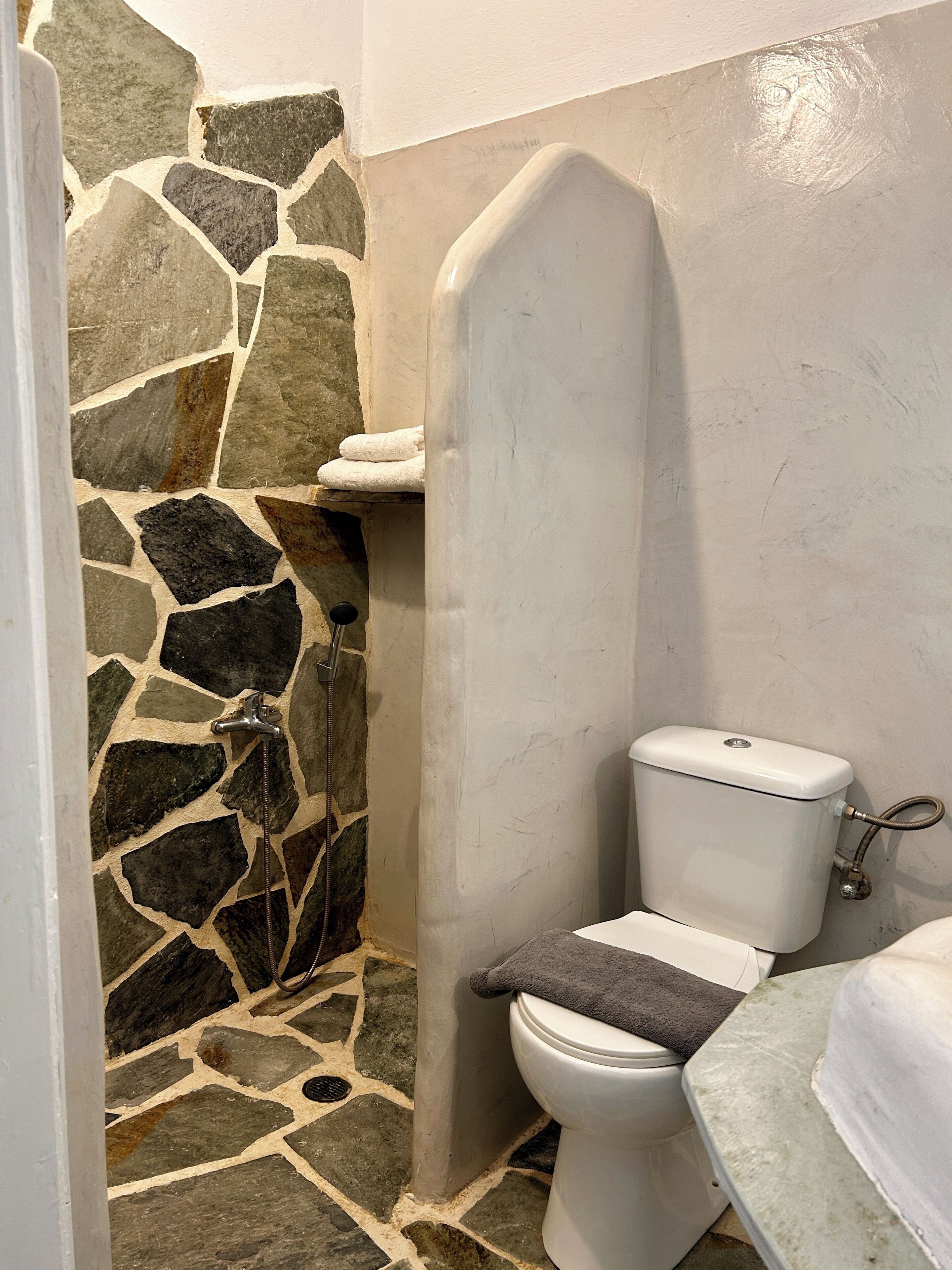 A bathroom with a stone wall, a toilet, and a shower area.