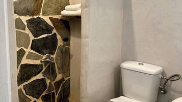 A bathroom with a stone wall, a toilet, and a shower area.