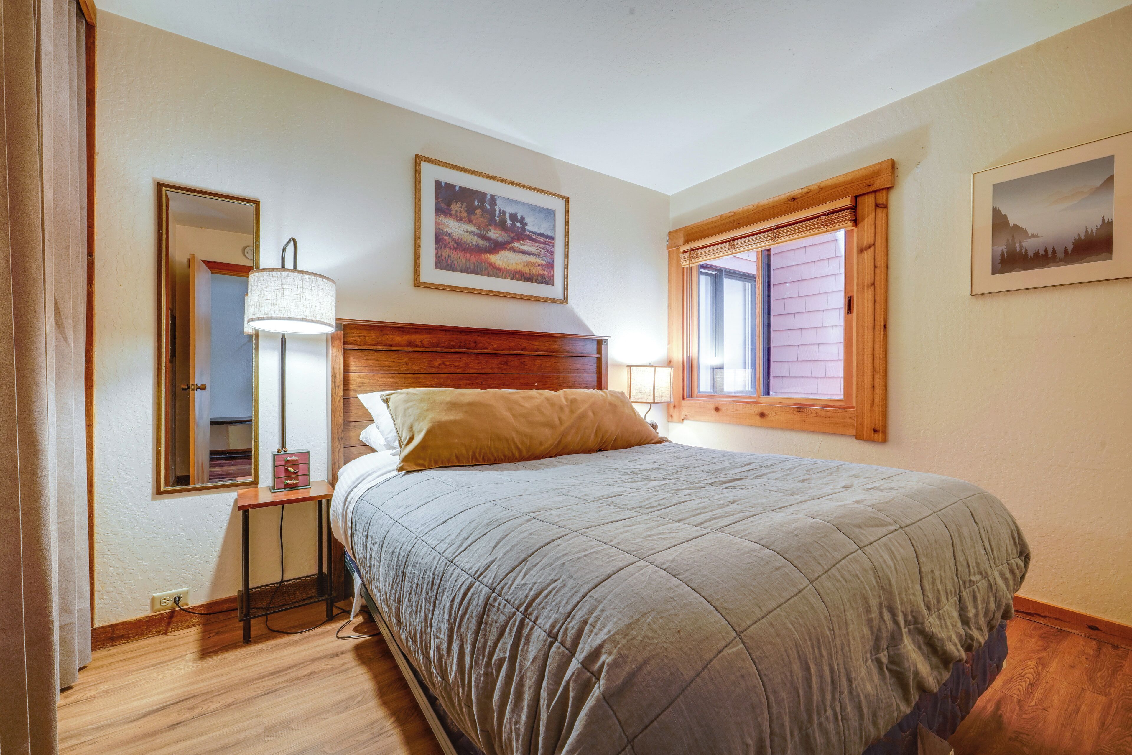 A bedroom with a bed, a bedside table, a lamp, a mirror, and two framed pictures on the wall.