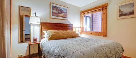 A bedroom with a bed, a bedside table, a lamp, a mirror, and two framed pictures on the wall.