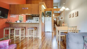 Una cocina compacta con taburetes de madera, un comedor con mesa y sillas, y un televisor montado en la pared.