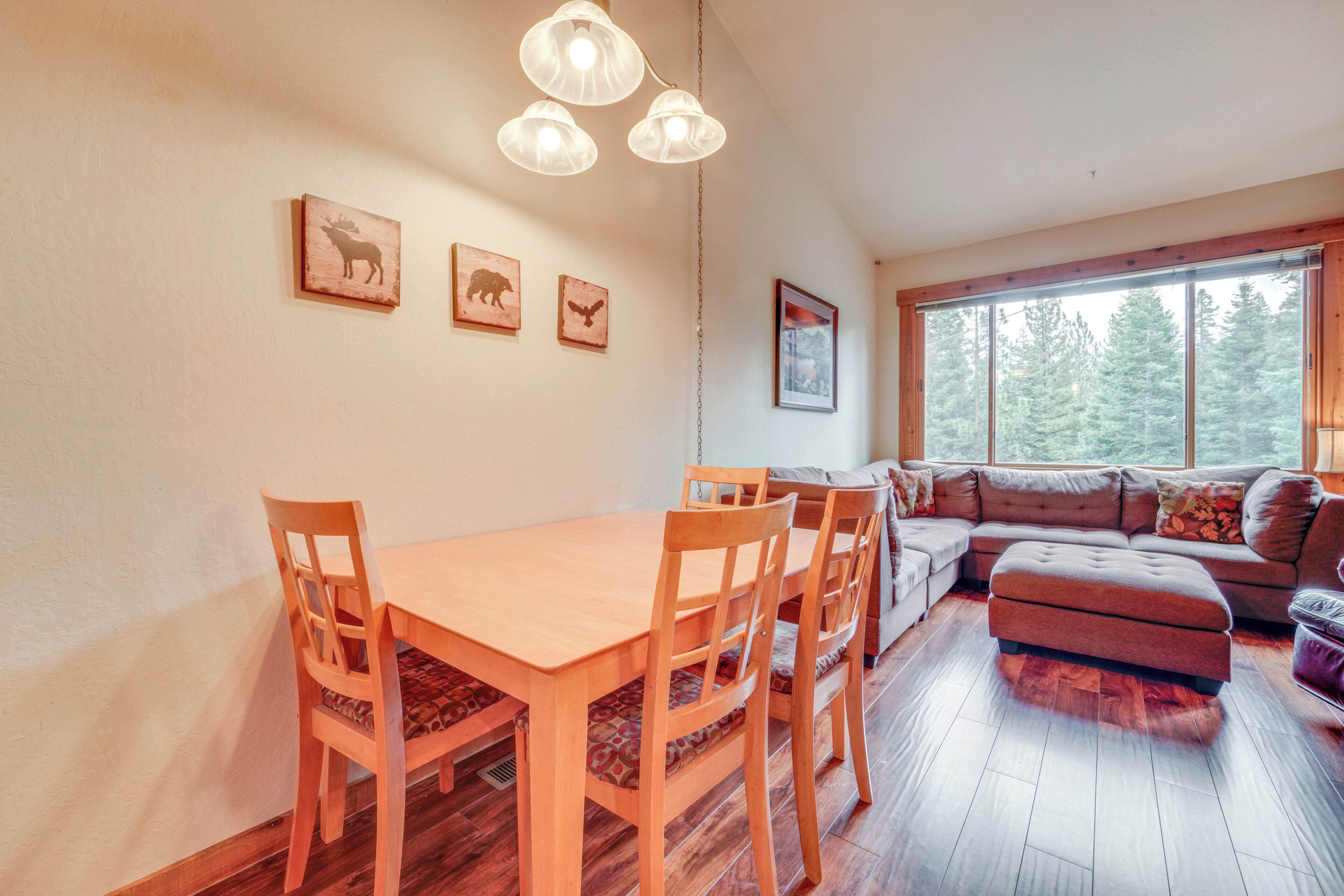 A dining area with a wooden table and chairs, a sofa, and a large window with a view of trees.