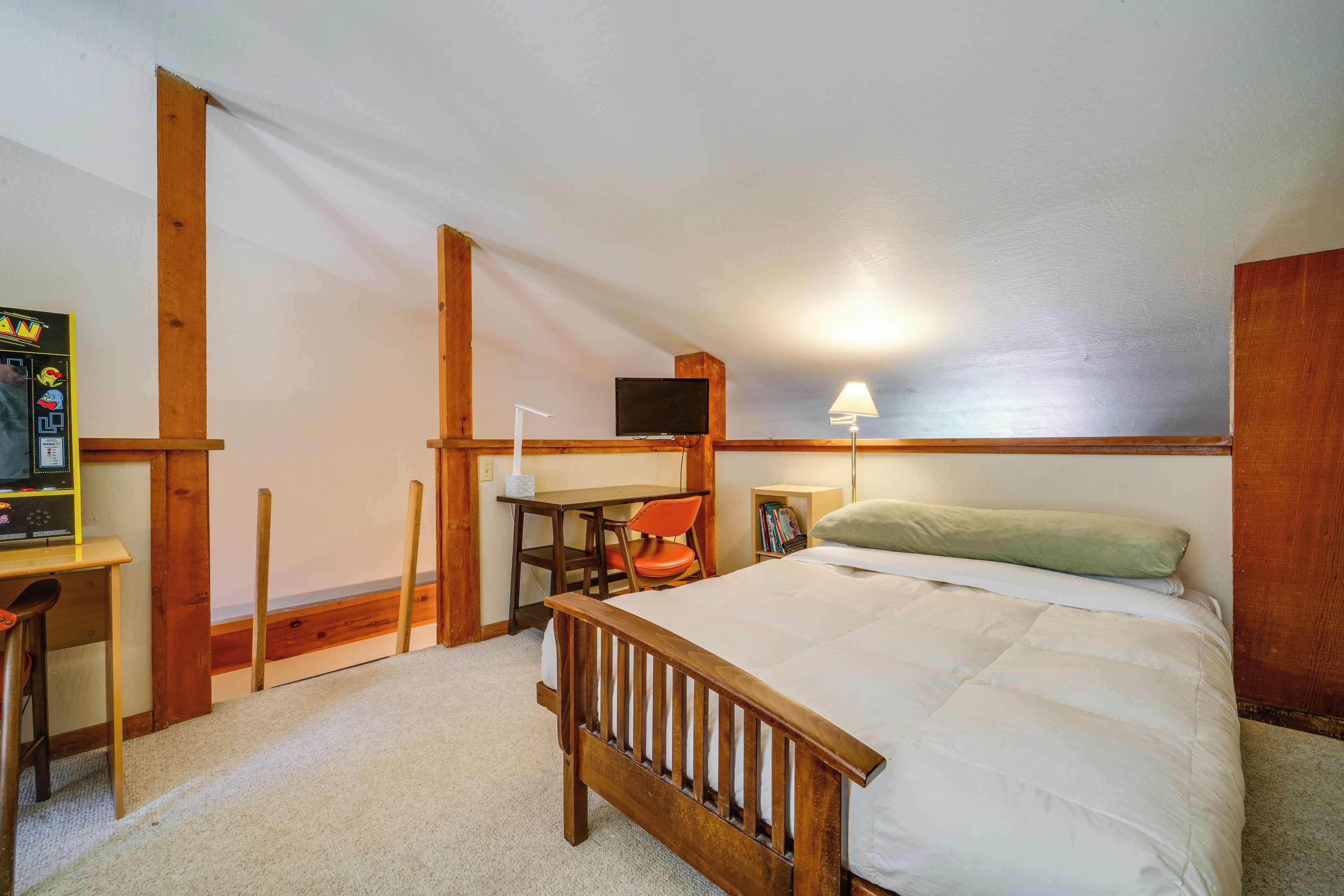 A bedroom with a wooden bed, a desk, a chair, a television, and a lamp.