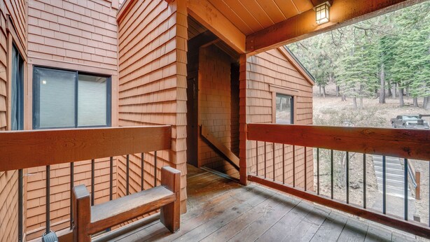 Una cabaña de madera con balcón, banco y vistas del bosque circundante.