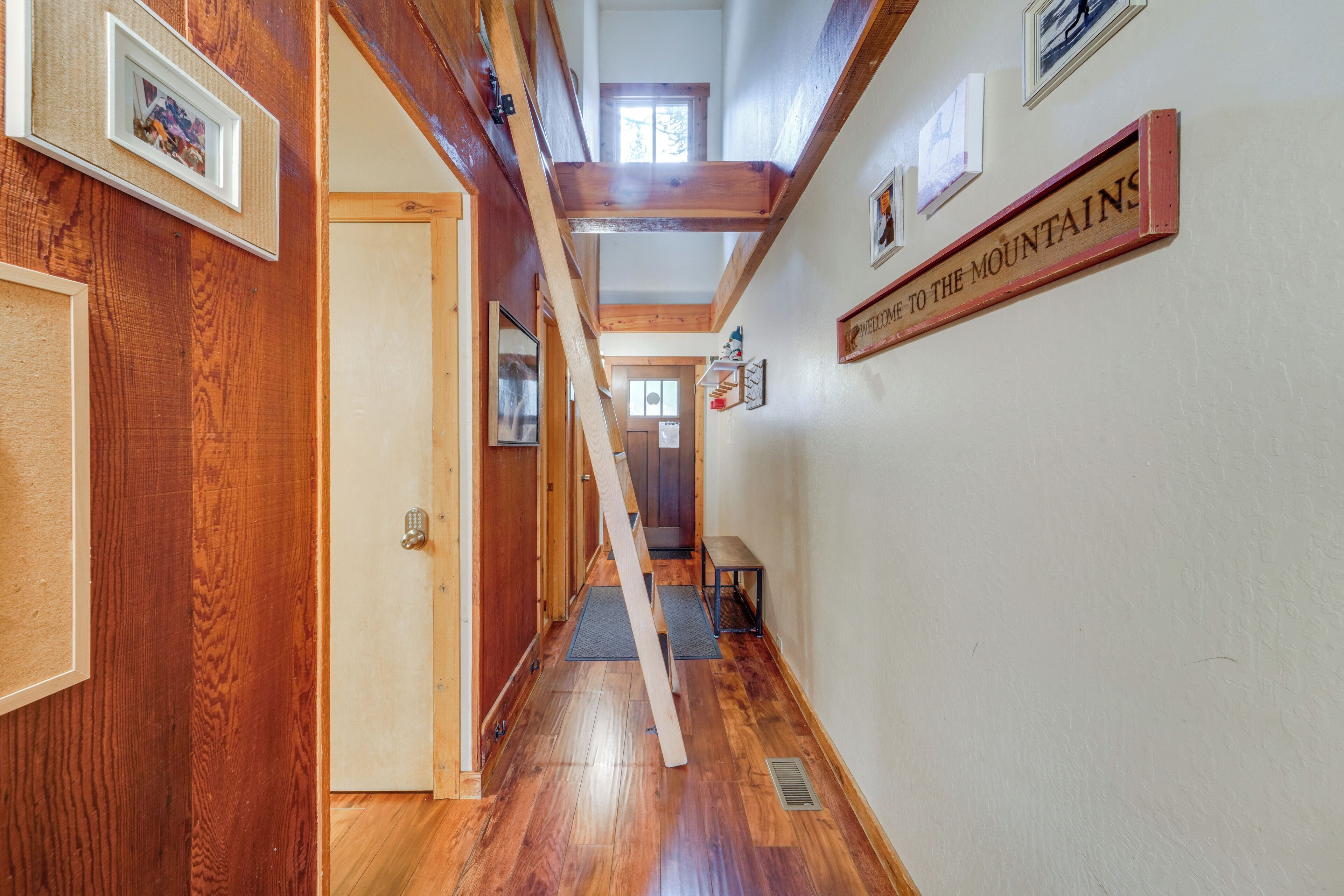 A wooden hallway with a sloped ceiling, a welcome sign, and framed pictures on the walls.