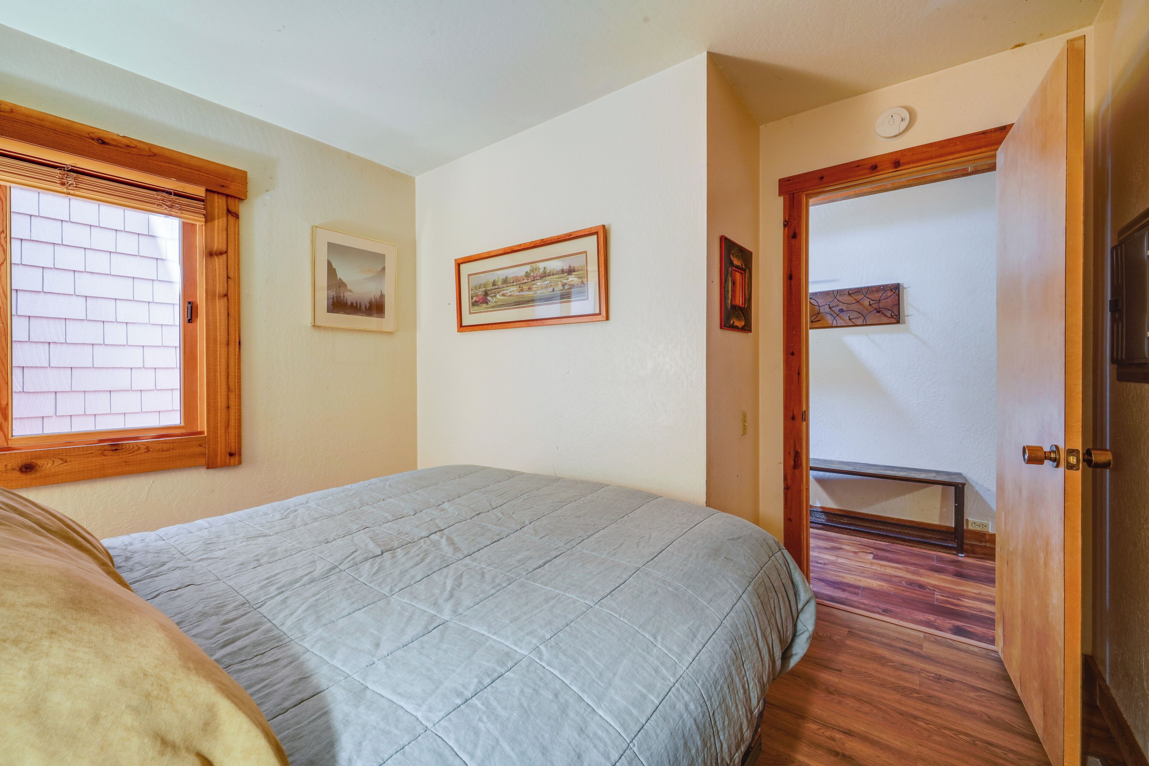 A bedroom with a bed, a window, a door, and a hallway leading to another room.