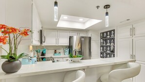 Une cuisine moderne avec des armoires blanches, des appareils en acier inoxydable, un îlot central doté de tabourets de bar et une lucarne.