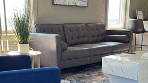 Ein Wohnzimmer mit grauem Sofa, blauem Sessel, Couchtisch und einem großen abstrakten Gemälde an der Wand.