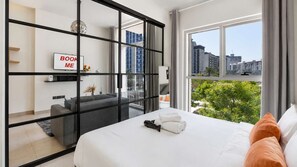 A modern hotel room with a large bed, a sofa, a desk, and a view of the cityscape.