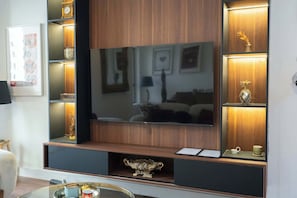 Uma sala de estar moderna com uma televisão de tela plana grande, painéis de madeira e objetos decorativos em prateleiras.