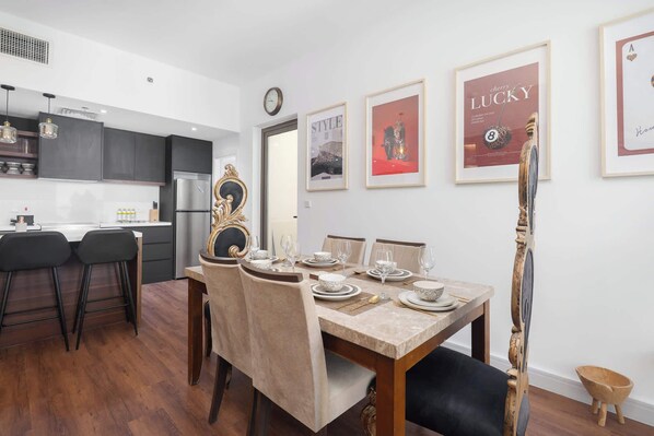 Un comedor con una mesa de madera dispuesta para cuatro, un reloj en la pared y obras de arte enmarcadas sobre la mesa.