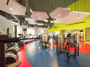 Un gimnasio con equipamiento cardiovascular, máquinas de pesas y suelo de colores.