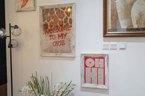 A wall with various framed artworks, including a newspaper-style print with 'HELLO MTV' and a red 'OH' sign.