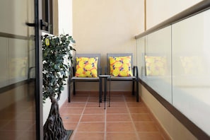 A balcony with two chairs and a small table, a potted plant, and a tiled floor.