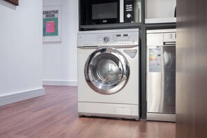A compact washer and dryer unit with a control panel and a digital display, placed in a room with wooden flooring and a white wall.