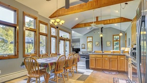 A spacious kitchen with wooden cabinets, a dining area with a table and chairs, and large windows allowing natural light. - Riverfront Home w/ Hot Tub Near Killington Resort (Bridgewater Corners)