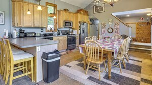 A spacious kitchen with wooden cabinets, a large island, and a dining area with a table and chairs. - Riverfront Home w/ Hot Tub Near Killington Resort (Bridgewater Corners)
