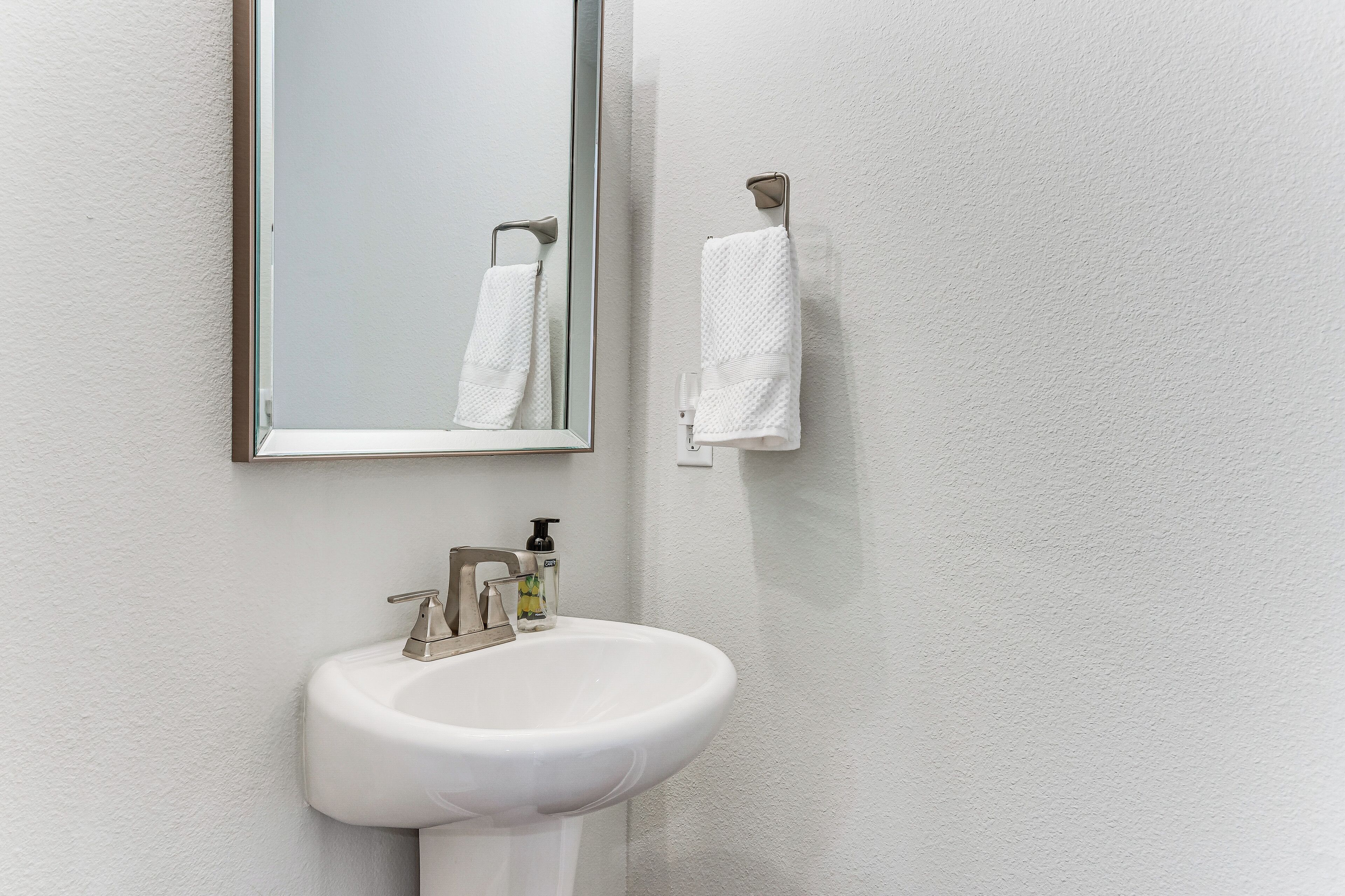 Un baño con un lavamanos blanco, un espejo y dos toallas blancas colgadas en la pared.
