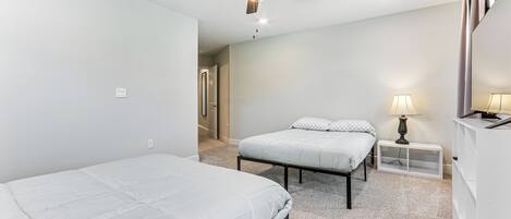 A room with two beds, a ceiling fan, a nightstand with a lamp, and a white wardrobe.
