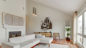 Un salon moderne avec un canapé d’angle blanc, une cheminée et des œuvres d’art accrochées aux murs.