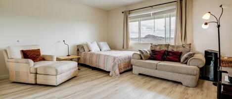 A spacious living room with a sofa set, a bed, and a large window with curtains.