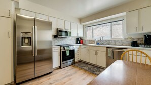 Una cucina moderna con elettrodomestici in acciaio inossidabile, mobili bianchi e un'ampia finestra che offre luce naturale.