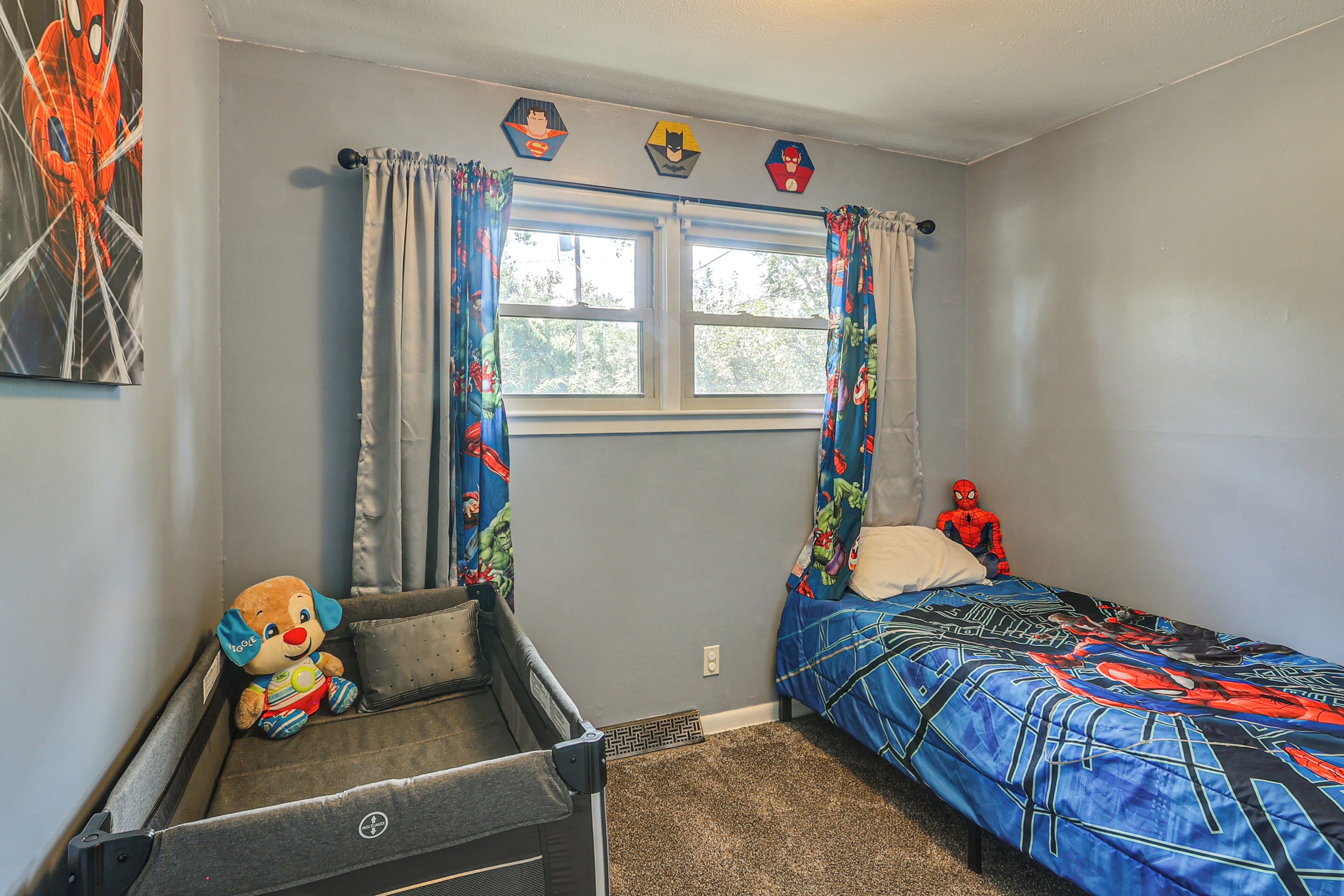 A bedroom with a bed, a small desk, a toy, and a window with curtains.