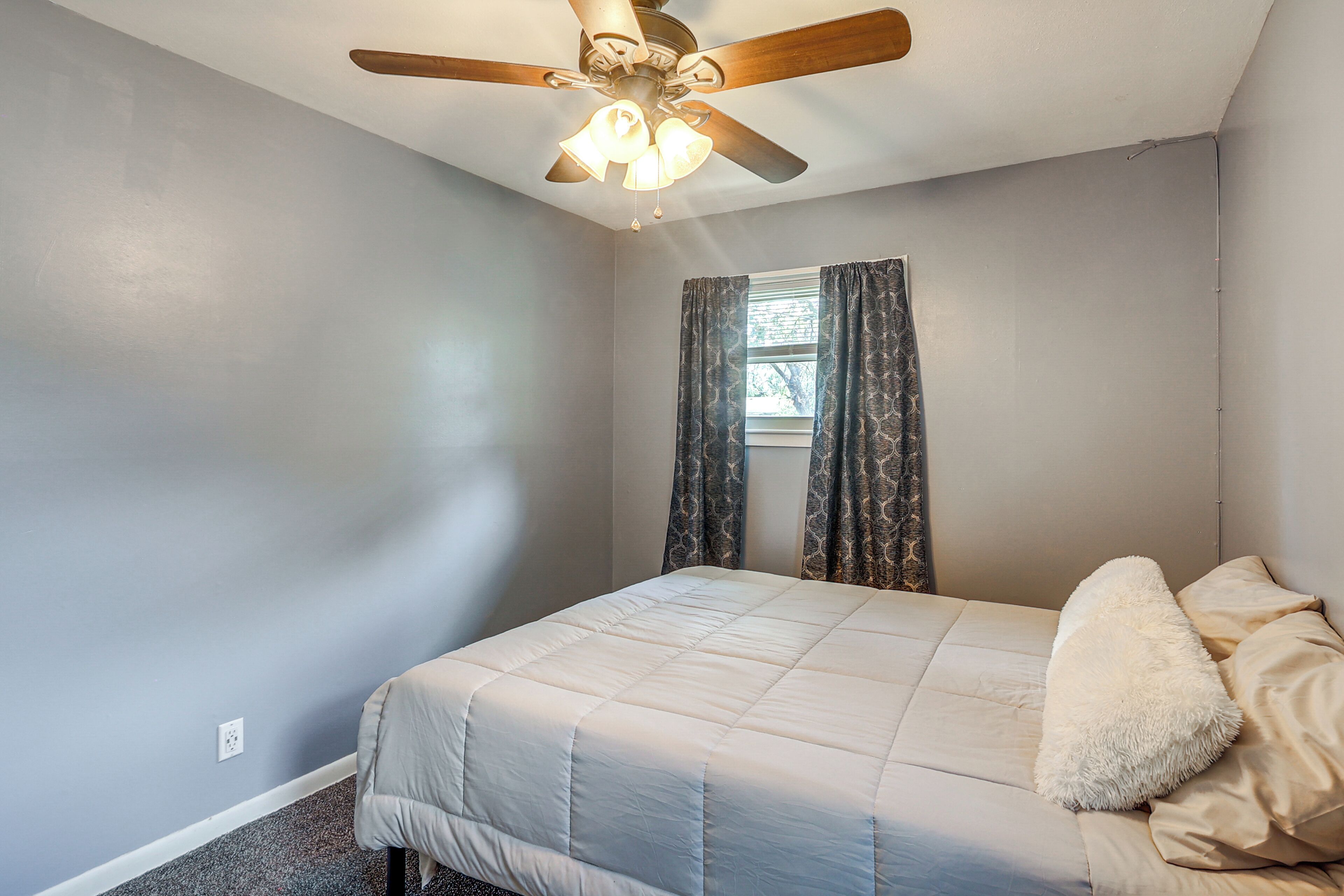 Une chambre à coucher avec un lit, un ventilateur de plafond et une fenêtre avec des rideaux.