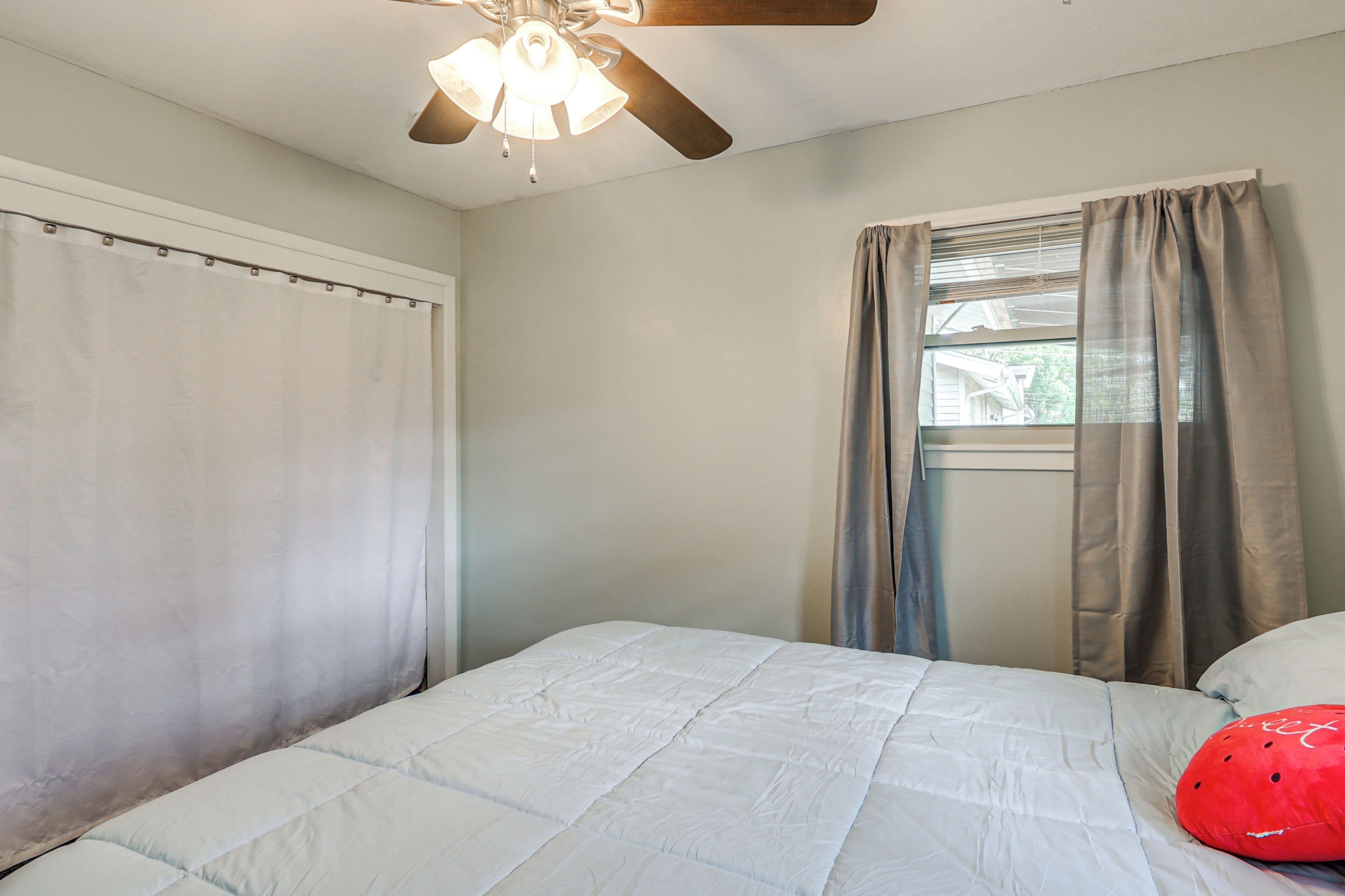 A bedroom with a bed, a ceiling fan, and a window with curtains.
