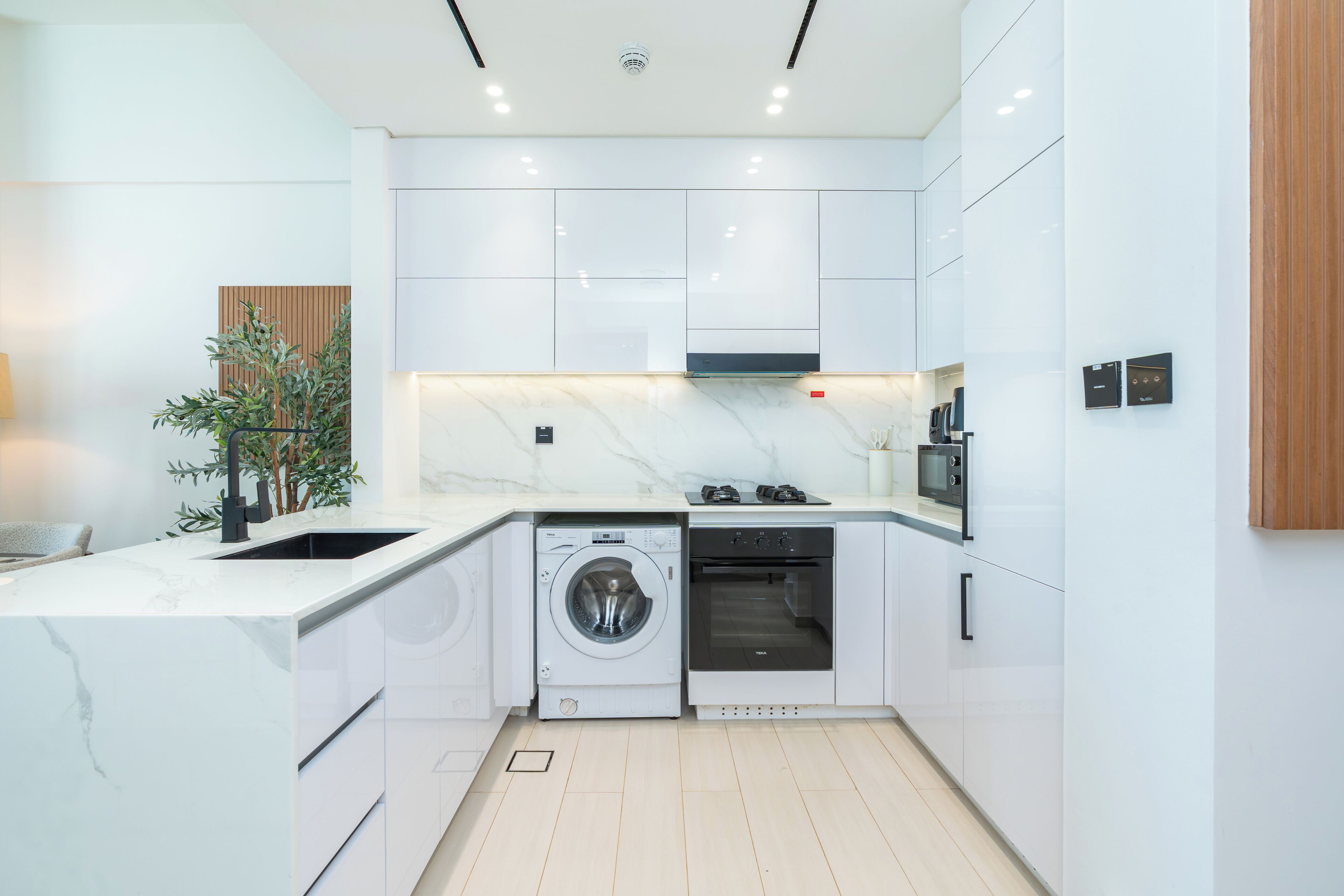 A modern kitchen with white cabinetry, a built-in washing machine, an oven, and a microwave.