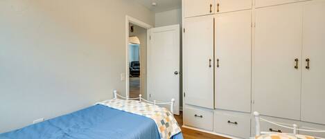 A bedroom with two single beds, a wardrobe, and a door leading to another room.