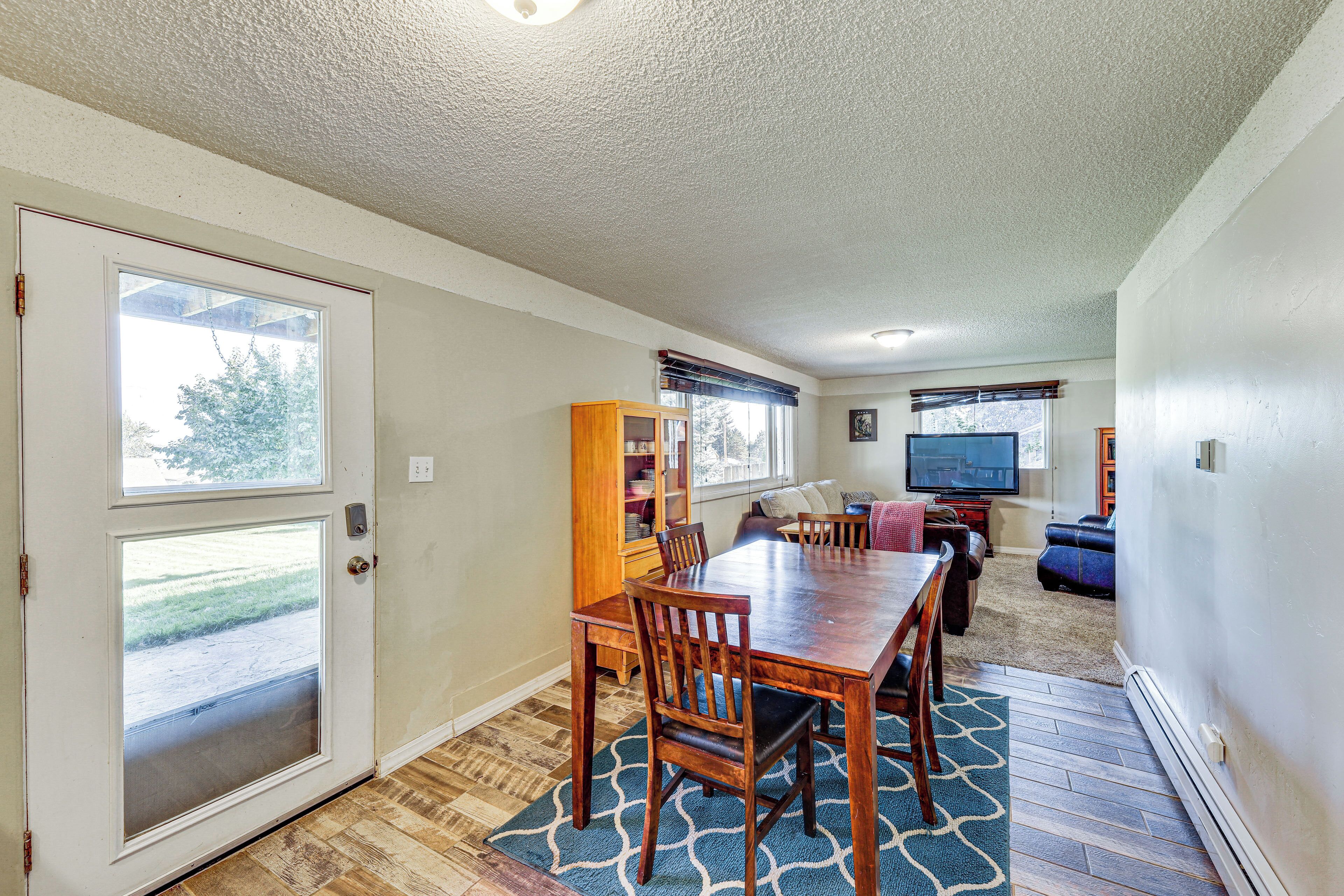 A dining area with a wooden table and chairs, a bookshelf, and a television in a living room with a view of the outdoors.